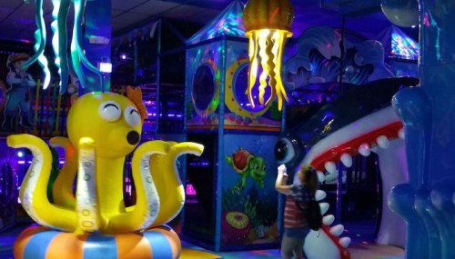 A colorful indoor play area featuring a yellow octopus and a shark, with vibrant lights and playful decorations.