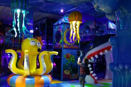 A colorful indoor play area featuring an octopus, jellyfish, and a shark, with vibrant lights and playful decorations.
