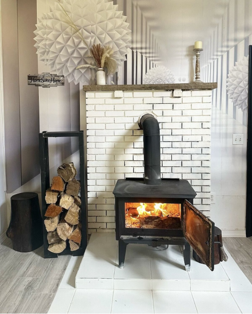 A cozy fireplace with a wood stove, stacked logs, and decorative wall elements in a warm, inviting room.