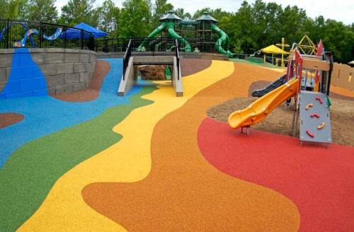 Colorful playground with slides and climbing structures, featuring vibrant rubber flooring in blue, yellow, and red.