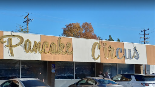 Sign for "Pancake Circus" on a building, with trees and parked cars in the foreground.