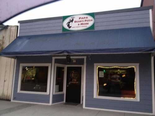 Exterior of Papa Bear's Pizza & More, featuring a blue building with a sign and awning, and illuminated windows.