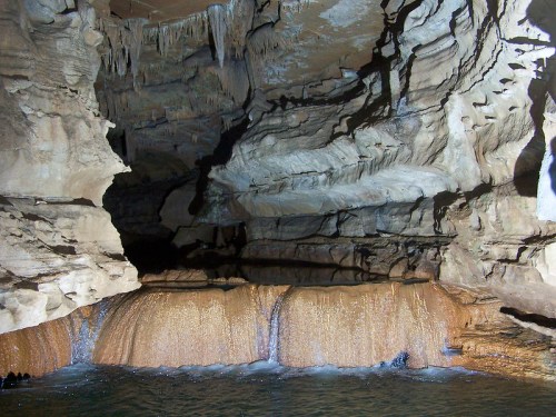 A dark cave interior with textured rock formations and a small waterfall flowing into a pool of water.