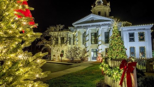 A beautifully lit heritage museum with festive decorations, surrounded by Christmas trees and holiday lights at night.
