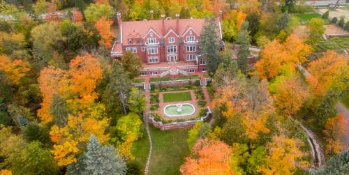 Aerial view of a large, historic mansion surrounded by vibrant autumn foliage and a manicured garden.