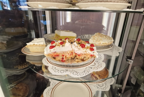 A glass display case filled with various pies and desserts, including a cherry-topped pie in the foreground.