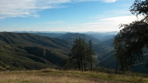 A scenic view of rolling mountains under a blue sky, with trees in the foreground and valleys stretching into the distance.
