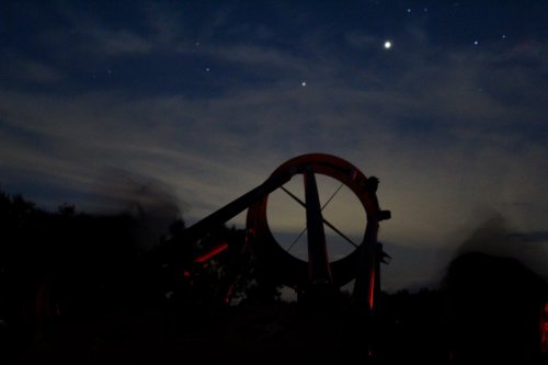 A silhouette of a large wheel against a night sky filled with stars and wispy clouds.