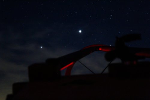 A telescope silhouette against a starry night sky, with bright celestial objects visible.