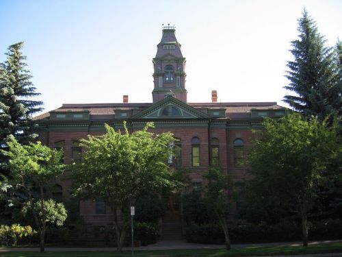 Historic brick building with a tower, surrounded by trees and a clear blue sky.