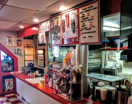 A cozy pizza shop interior featuring a menu board, counter, and vintage decor with a playful atmosphere.
