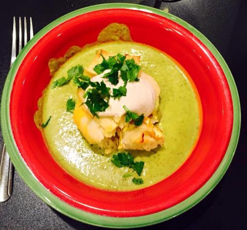 A vibrant bowl of green soup topped with a piece of chicken and fresh cilantro, served in a colorful dish.
