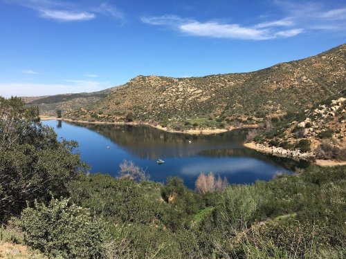 A serene lake surrounded by hills and greenery under a clear blue sky, with a few boats on the water.