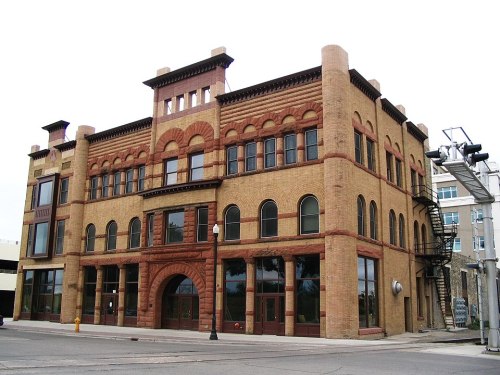 Historic brick building with arched windows and decorative elements, featuring a prominent entrance and fire escape.