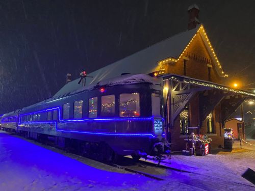 A beautifully lit train station at night, adorned with festive lights and surrounded by falling snow.