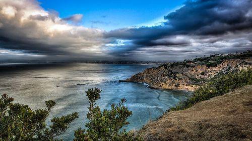 A scenic coastal view with cliffs, a calm sea, and dramatic clouds in the sky.