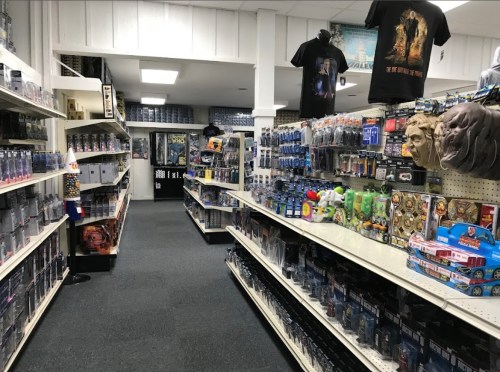 A wide aisle in a store filled with shelves of toys, collectibles, and merchandise, with posters and shirts hanging above.