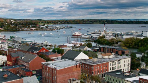 Aerial view of a coastal town with boats in the harbor, colorful buildings, and a cloudy sky.
