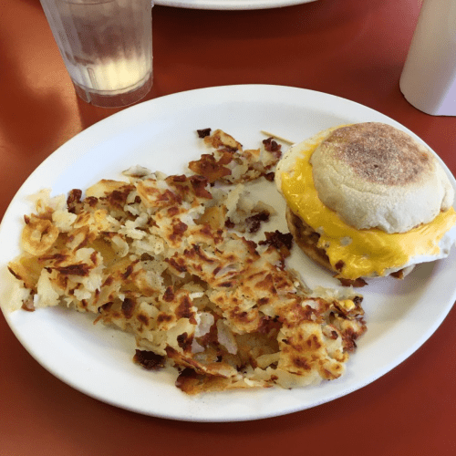 A plate with crispy hash browns and a breakfast sandwich with cheese on a toasted English muffin.