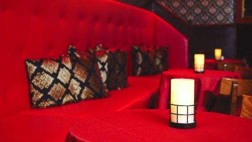 Cozy restaurant interior with red seating, decorative pillows, and candlelit tables.