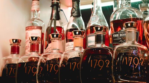 A collection of whiskey bottles on a shelf, featuring various brands and labels, with rich amber liquid visible.