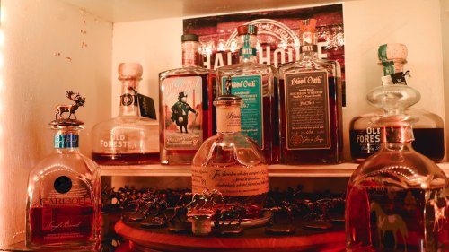 A collection of various whiskey bottles displayed on a shelf, with decorative figurines in front.