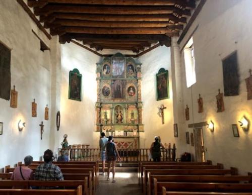 Interior of a historic chapel with wooden beams, religious artwork, and visitors admiring the space.