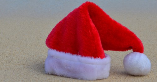 A plush red and white Santa hat resting on the warm sand of a beach.