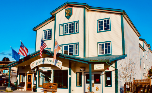 A three-story building with flags outside, featuring a sign that reads "Scandia House" in a sunny setting.