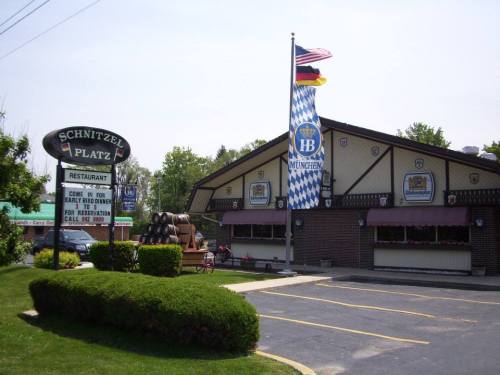 Exterior of Schnitzel Platz restaurant featuring a sign, flags, and a landscaped parking area.