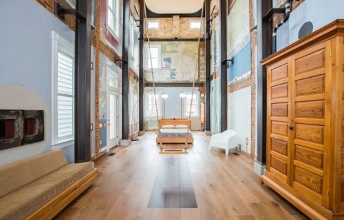 Spacious interior with high ceilings, exposed brick walls, wooden furniture, and large windows for natural light.