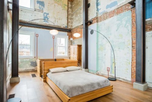 A modern bedroom with a wooden bed, large windows, and exposed brick walls, featuring a minimalist design.