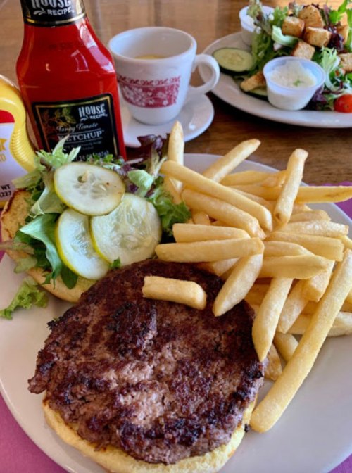 A plate with a burger topped with lettuce and pickles, served with fries, ketchup, and a side salad in the background.