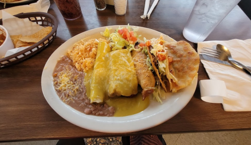 A plate of Mexican food featuring enchiladas, rice, refried beans, salad, and a crispy taco.
