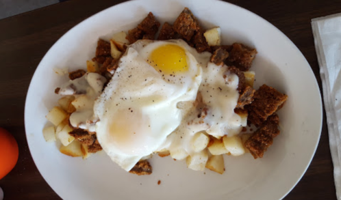 A plate of breakfast featuring two fried eggs on a bed of diced potatoes and crispy bread pieces.