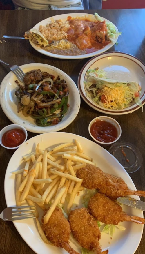 A table with two plates of food: one with fried shrimp and fries, the other with rice, tacos, and salad. Ketchup on the side.