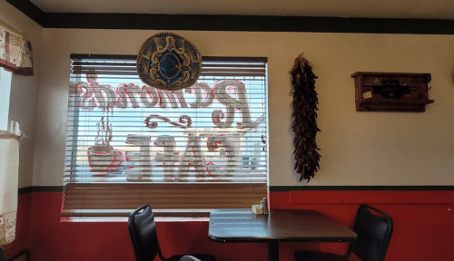 Interior of a cafe with a window displaying "Restaurant Cafe," decorated with a chili pepper and a wall hanging.