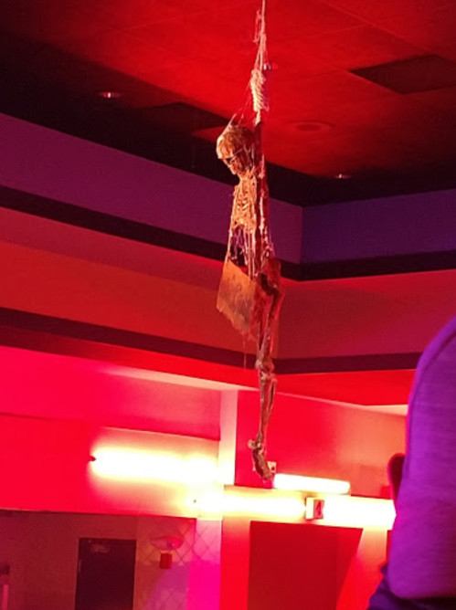 A hanging skeleton decoration in a dimly lit room with colorful lighting.