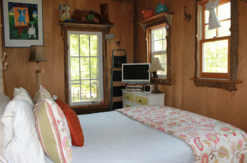 Cozy bedroom with a bed, decorative pillows, a desk, and windows letting in natural light.
