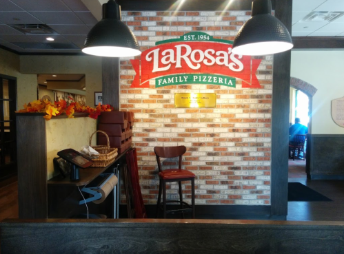 Interior of LaRosa's Family Pizzeria featuring a brick wall with the restaurant's logo and a wooden chair.