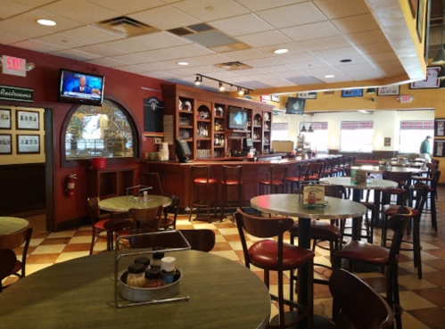 Interior of a restaurant featuring a bar, tables, and a TV, with a warm, inviting atmosphere.