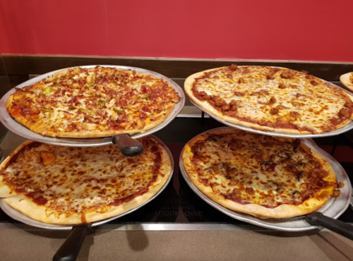Four pizzas on metal trays, featuring various toppings like cheese, pepperoni, and vegetables, displayed on a counter.