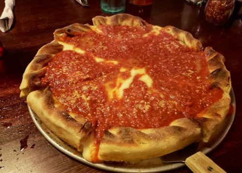 A deep-dish pizza topped with marinara sauce and sprinkled with cheese, served on a metal tray.