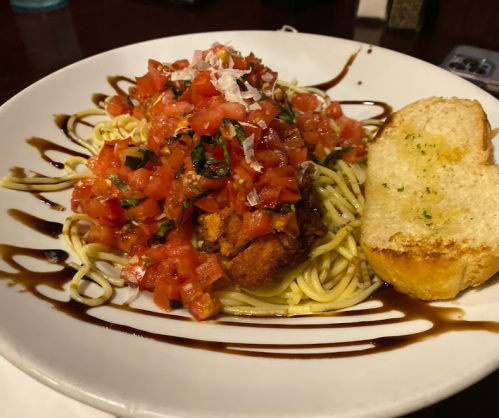 A plate of pasta topped with fresh tomato basil salsa, served with a slice of garlic bread.