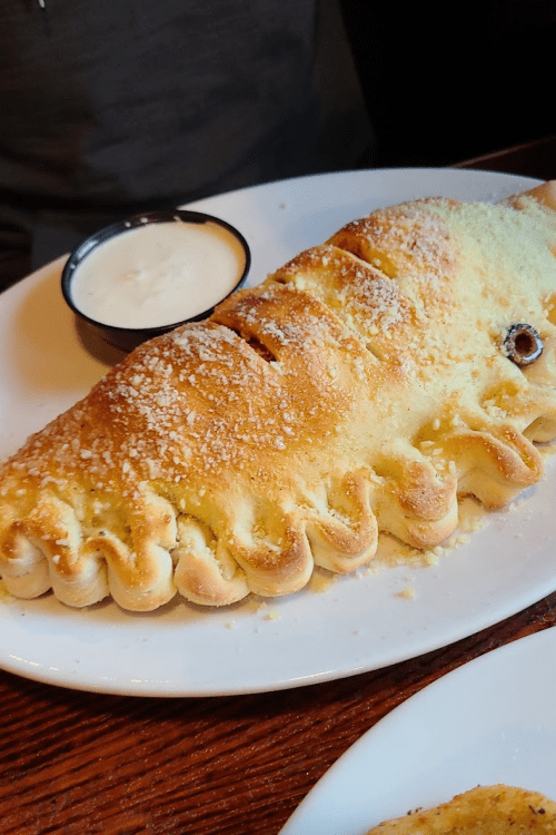 A large calzone topped with cheese, served on a plate with a side of dipping sauce.