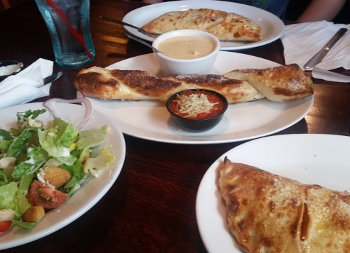 A table setting with a salad, a bowl of soup, and two stuffed calzones on white plates.