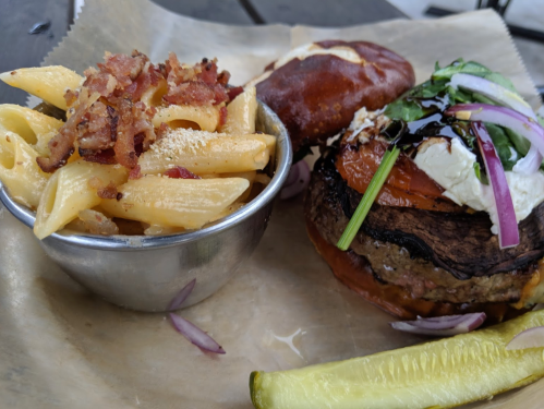 A plate featuring a burger with toppings, a side of macaroni and cheese, and a pickle slice.