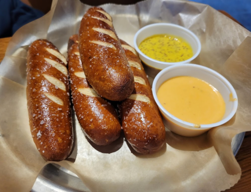 A plate of soft pretzel sticks with two dipping sauces, one yellow mustard and one creamy cheese.