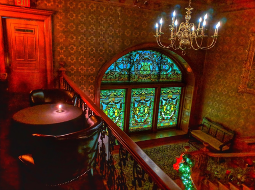 A dimly lit staircase with a stained glass window, chandelier, and a small table set for two.