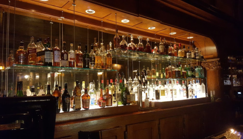 A well-stocked bar with various bottles of liquor displayed on glass shelves under warm lighting.